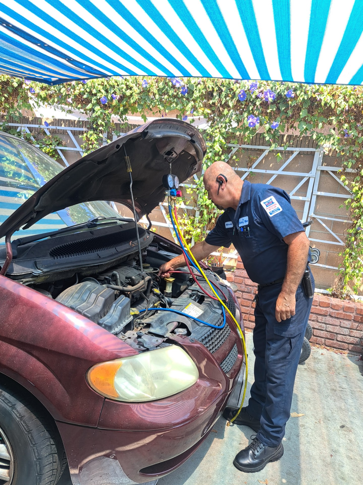 The Battery Man connecting automotive A/C manifold gauges under the hood of a customer vehicle.