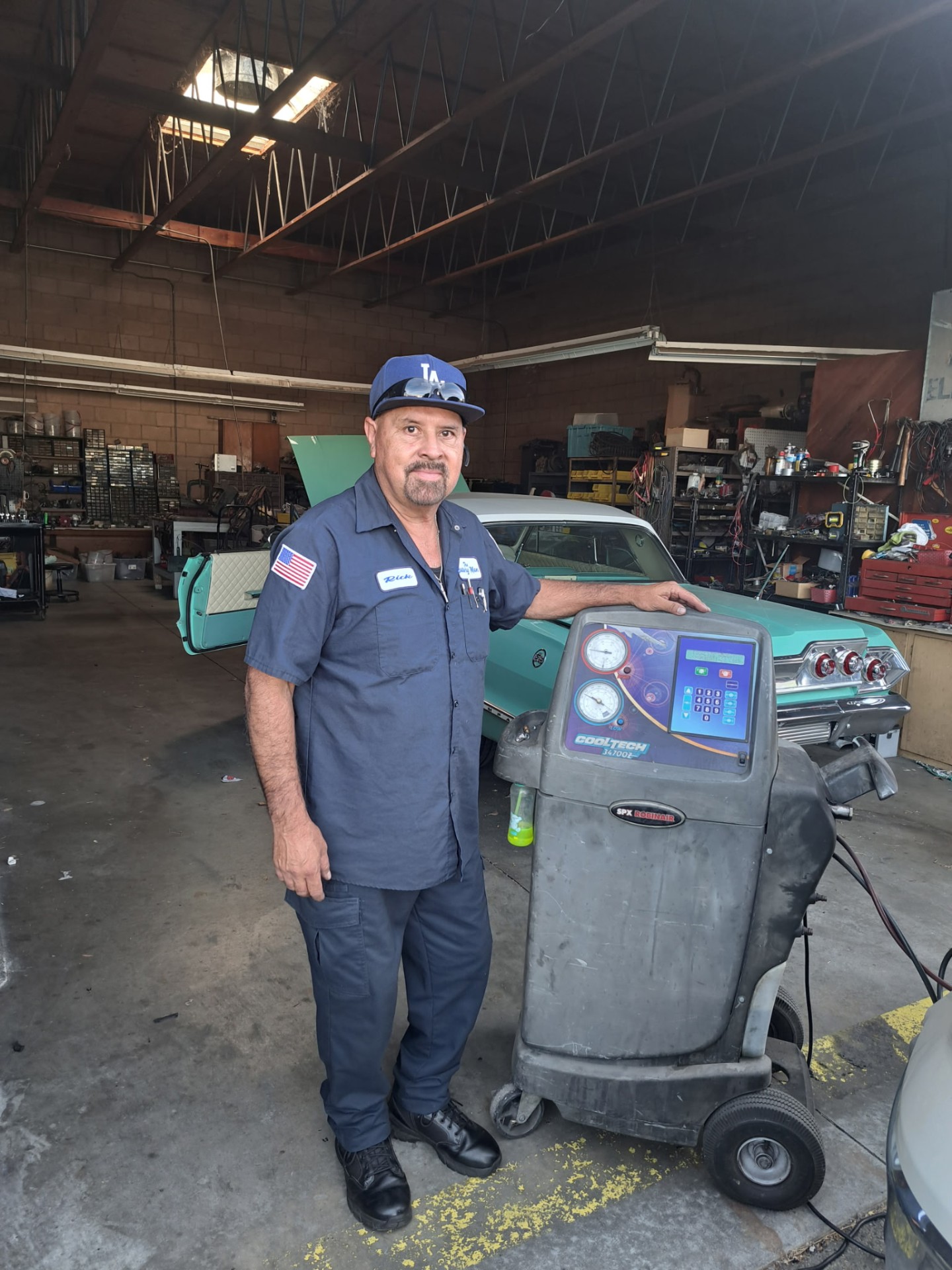 Rick in the shop next to an A/C recovery machine beside a classic car